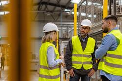 Conflict resolution is an important workplace soft skill Three workers in safety vests and hard hats talking in a warehouse