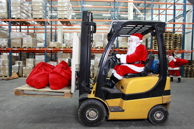 Santa using a forklift for sack of gifts in a warehouse