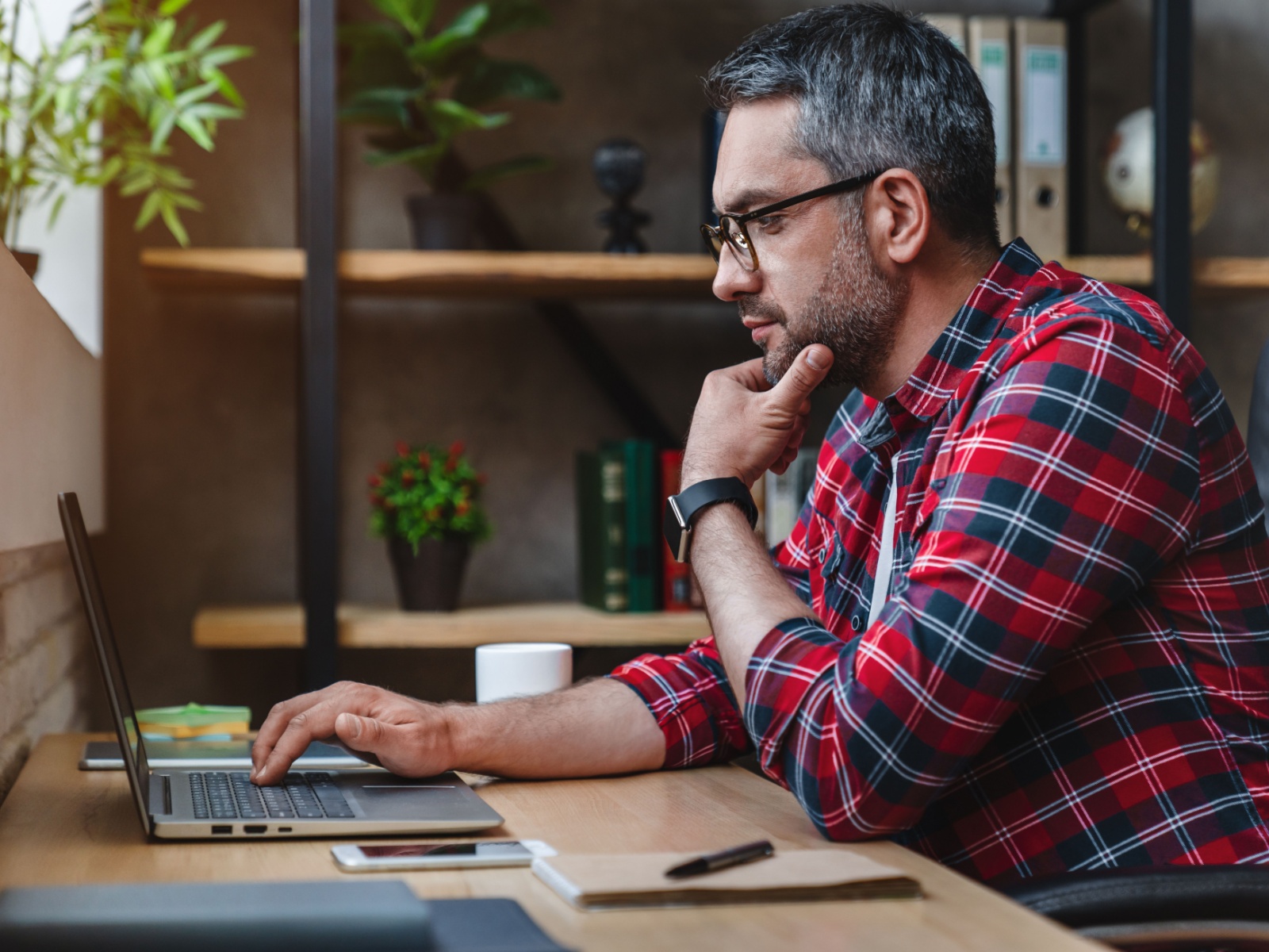 A man in a flannel shirt researching on a computer