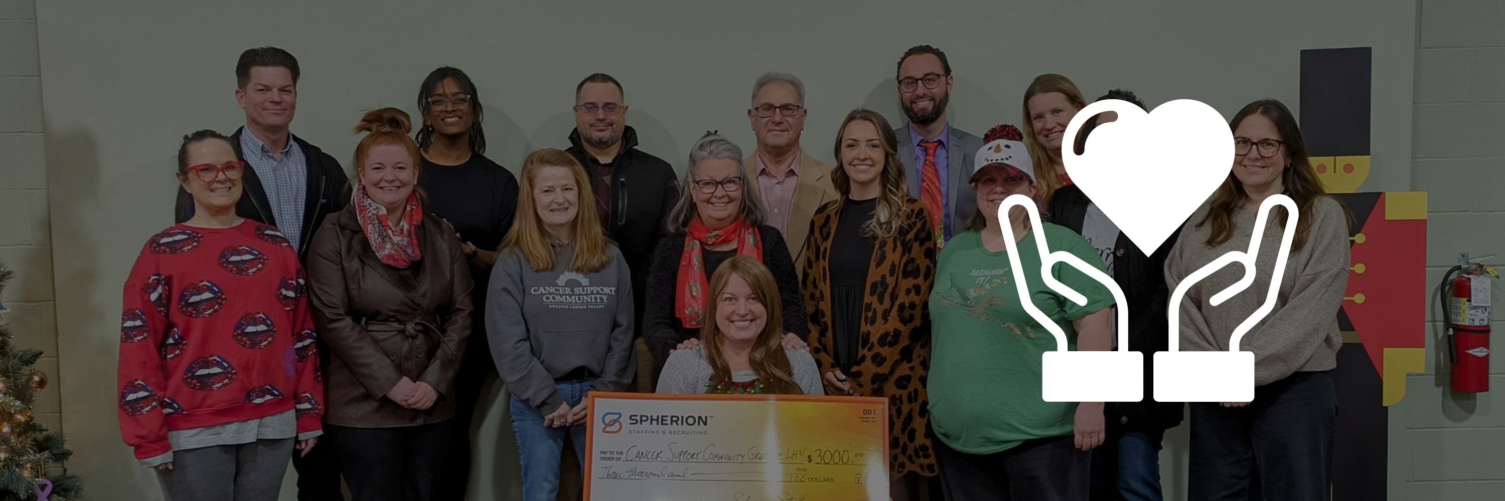 A photo of a grop of people presenting a giant check with a white heart and hands logo