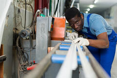 A man in a blue apron focuses on measuring a metal beam